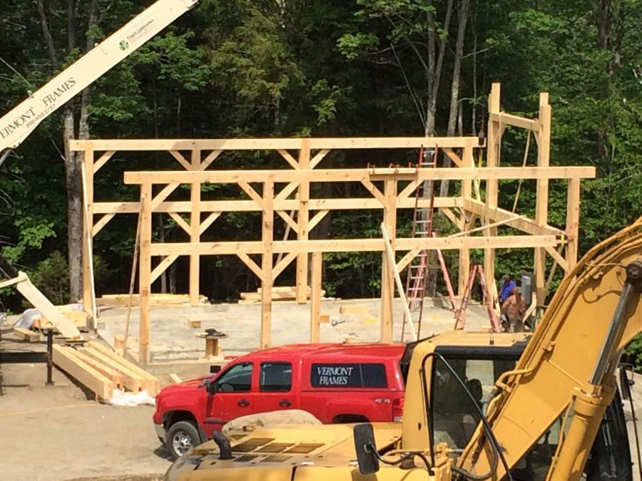 Timber frame beam structure of a barn with a crane and other construction vehicles